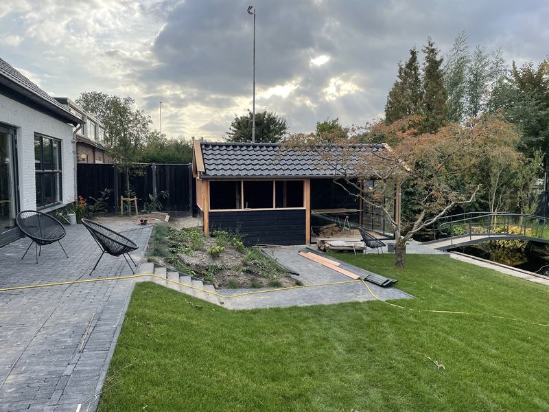 Aangelegde tuin met gazon, bestrating, traptreden en overkapping aan het water